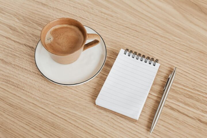 木の机に置かれたノートとペン、温かいコーヒー。自分の目標を書き出すイメージ