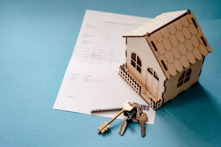 木製の家の模型と鍵、契約書。住宅ローンを借りる手続きのイメージ